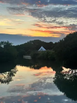 a sunset over a river with a building in the distance at Lakeside Glamping Firecrest in Saint Columb Major