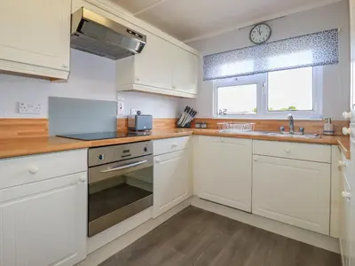 a kitchen with white cabinets and a sink and a window at Lowen Lodge in Padstow