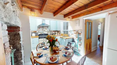a kitchen with a wooden table and chairs and a kitchen with white appliances at St Ives Bubblegum Cottage in St Ives