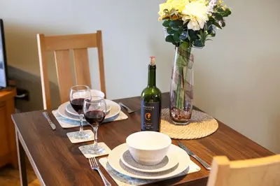 a wooden table with a bottle of wine and a vase of flowers at The Tractor Shed, a romantic barn retreat on the edge of Falmouth in Budock Water