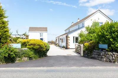a white house with a stone wall next to a street at The Tractor Shed, a romantic barn retreat on the edge of Falmouth in Budock Water