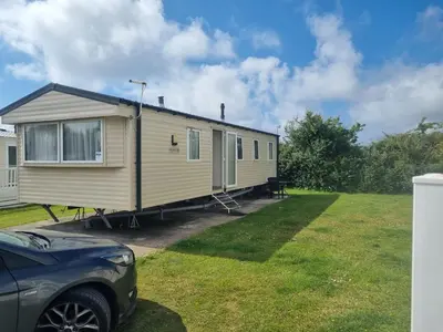 a yellow caravan parked in a yard with a car at Chapmans Holiday Home Newquay in Newquay