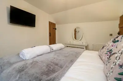a bedroom with a large white bed with a flat screen tv at Bumblebee Cottage in Bodmin