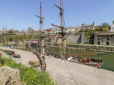 a tall ship docked in a river next to a building at Bumblebee Cottage in Bodmin
