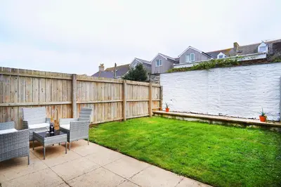 a backyard with a fence and a lawn with chairs at Bredon Court by Signature Stays - Modern - Beach - Parking in Newquay