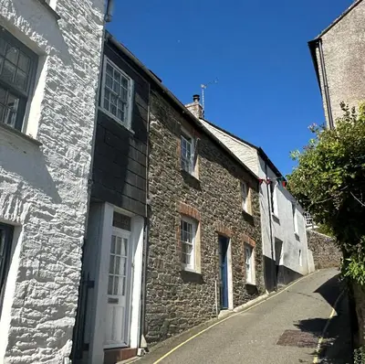 a stone building with a white door on a street at Seaforth - Fisherman's Cottage in Gorran Haven