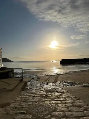 a beach with the sun rising over the water at Seaforth - Fisherman's Cottage in Gorran Haven