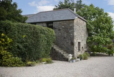 a stone building with a hedge next to a house at The Hay Loft in Camborne