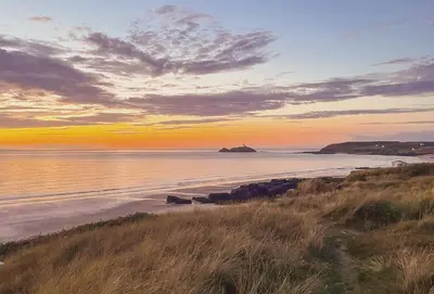 a view of a beach at sunset with the ocean at The Corner Cottage in Camborne