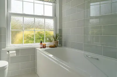 a white bathroom with a tub and a window at Sandpipers, Port Isaac Bay Holidays in Port Isaac