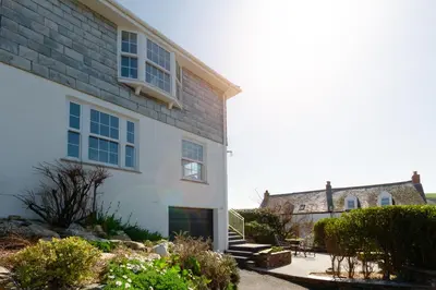 a white house with a building in the background at Sandpipers, Port Isaac Bay Holidays in Port Isaac