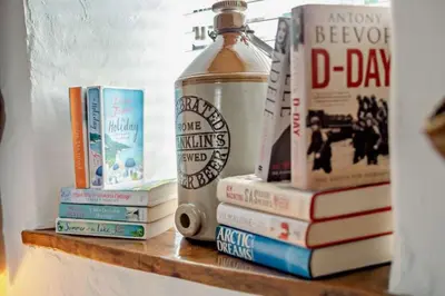 a shelf with books and a bottle on top of it at Nuthatch by Together Travel - Luxury Cornish Countryside Retreat in Bodmin