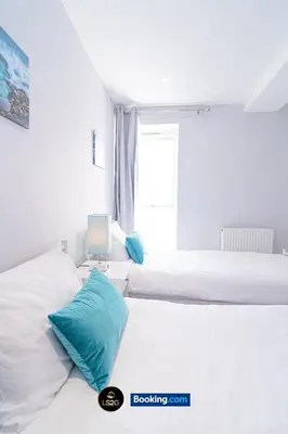 a white bedroom with two beds with blue pillows at Spacious 2 Bedroom Flat By LS2G Short Lets & Serviced Accommodation Greater London With Free WIFI in Newquay