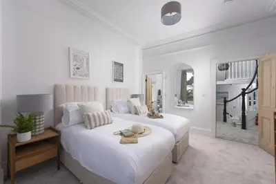 a white bedroom with a large bed and a table at The Elms in Uny Lelant