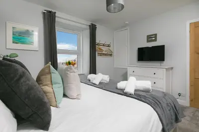a bedroom with a large white bed with a television at Benjamin's Bolthole in St Ives