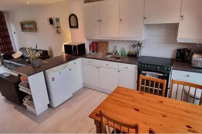 a kitchen with white cabinets and a table and a couch at 2 Bed Cottage Sleeps 5 - Pets Allowed in Newquay
