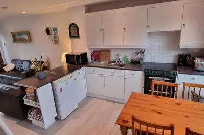 a kitchen with white cabinets and a table and a couch at 2 Bed Cottage Sleeps 5 - Pets Allowed in Newquay