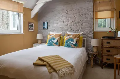 a bedroom with a large white bed with a stone wall at Zen Den Cornwall in Boscastle