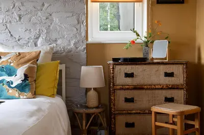 a bedroom with a bed with a dresser and a window at Zen Den Cornwall in Boscastle