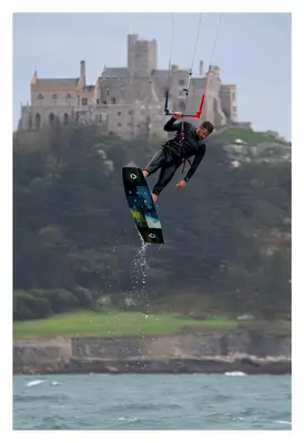 a man in the air on a surfboard in the water at Beach House Apartment, Across St Michaels Mount in Marazion
