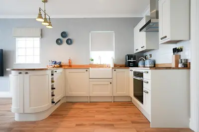 a kitchen with white cabinets and a wooden floor at Beach House Apartment, Across St Michaels Mount in Marazion