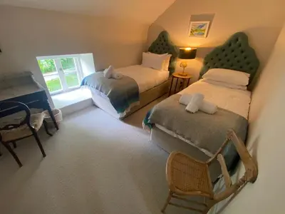 a bedroom with two beds and a chair and a window at Tregrylls Barton in Boscastle