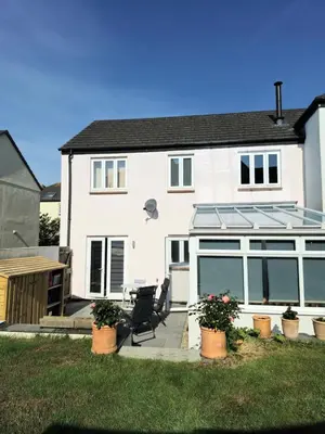 a white house with a large window and a chair at Cosy house on a quiet estate in Truro in Truro