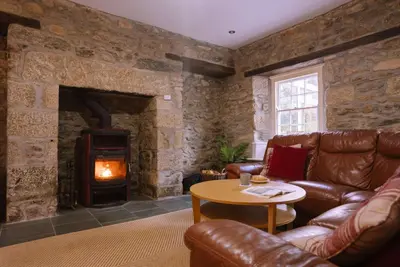 a living room with leather furniture and a stone fireplace at Beautiful Country Farmhouse Set In A Stunning Woodland With Pool, Sauna & Parking at 'The Old Farmhouse' in Ponsanooth