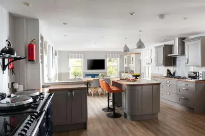 a kitchen with white cabinets and an island with a counter at Beautiful Country Farmhouse Set In A Stunning Woodland With Pool, Sauna & Parking at 'The Old Farmhouse' in Ponsanooth