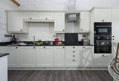 a white kitchen with white cabinets and black appliances at Rainbow Cottage in Liskeard