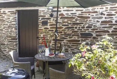 a table with chairs and an umbrella on a patio at Rainbow Cottage in Liskeard