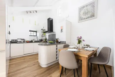 a white kitchen with a wooden table and chairs at Blackberry Barn in Liskeard