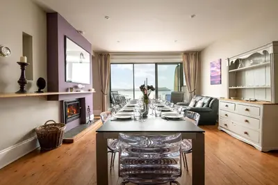 a long table in a living room with a fireplace at Atlantic View, North Cornwall seafront, 5* Gold in Polzeath