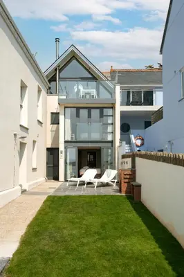 a glass house with a lawn in front of it at Atlantic View Coach House, North Cornwall seafront, 5 star Gold in Polzeath