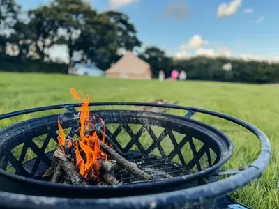 a fire pit with orange flames in a field at Furnished Bell Tent 1 in St Austell