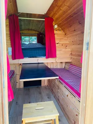 a inside of a wooden cabin with a bed and red curtains at Barrel Cabin 1 in St Austell