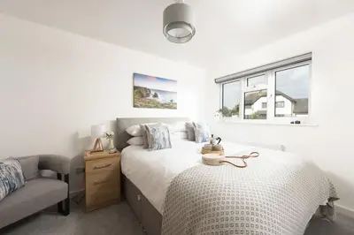 a white bedroom with a bed and a chair at Tre Lowen, Goonhavern, Perranporth - Free Parking - Free Wifi - Games Room in Perranporth