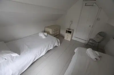 a white bedroom with two beds and a chair at Sea Haven in Port Isaac