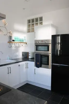 a kitchen with white cabinets and a black refrigerator at Flip Flop Flat, Sea Views, Short Stroll to Beaches in Newquay