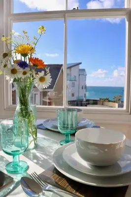 a table with plates and glasses and a vase of flowers at Flip Flop Flat, Sea Views, Short Stroll to Beaches in Newquay