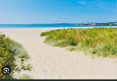 a sandy beach with grass and the ocean in the background at The Driftwood Den in Tywardreath