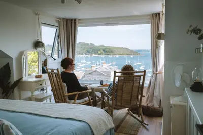 a woman sitting in a chair in a room with a window at Stunning High Street Townhouse With Sea Views & Parking at 'Tide View Townhouse' in Falmouth