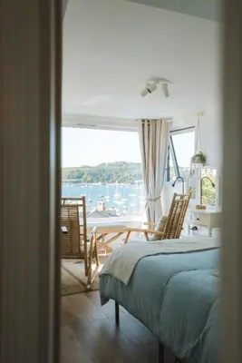 a bedroom with a bed and chairs and a large window at Stunning High Street Townhouse With Sea Views & Parking at 'Tide View Townhouse' in Falmouth