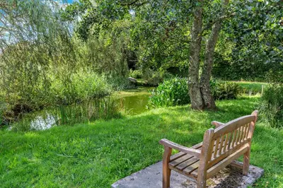 a wooden bench sitting in the grass near a pond at 2 Bed in Ruan High Lanes oc-r29865 in Ruan Lanihorne