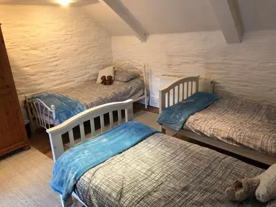 a bedroom with three beds with a teddy bear sitting on top at 17th Century Traditional Tintagel Farmhouse with Hot Tub in Treknow