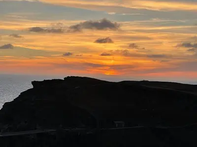 a sunset on a hill with the ocean in the background at 17th Century Traditional Tintagel Farmhouse with Hot Tub in Treknow