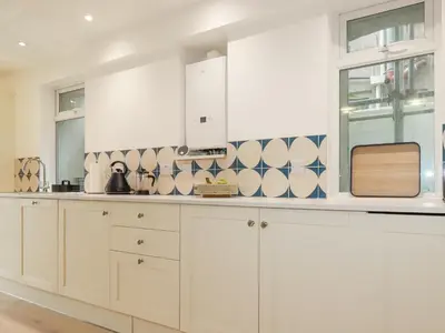 a kitchen with white cabinets and blue and white tiles at Serendib Cottage in Newquay