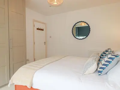 a bedroom with a white bed with a mirror on the wall at Serendib Cottage in Newquay