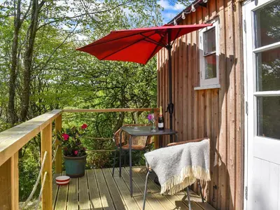 a red umbrella on a deck with a table at The Shepherds Hut At Rosewood House in Liskeard