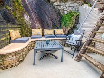 a patio with a bench and two chairs and a table at Charlie Wilcox Cottage in Polperro